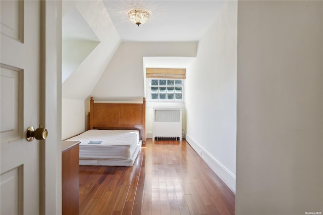 unfurnished bedroom featuring wood-type flooring, radiator heating unit, and vaulted ceiling