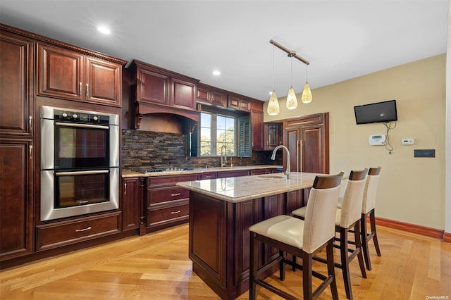 kitchen with light stone countertops, sink, stainless steel appliances, backsplash, and a kitchen island with sink