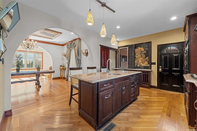 kitchen featuring pendant lighting, a breakfast bar, a kitchen island with sink, sink, and ornamental molding