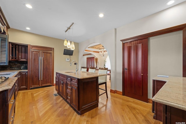 kitchen with sink, hanging light fixtures, paneled fridge, a kitchen island, and light wood-type flooring