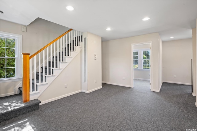 unfurnished living room featuring a wealth of natural light and dark carpet