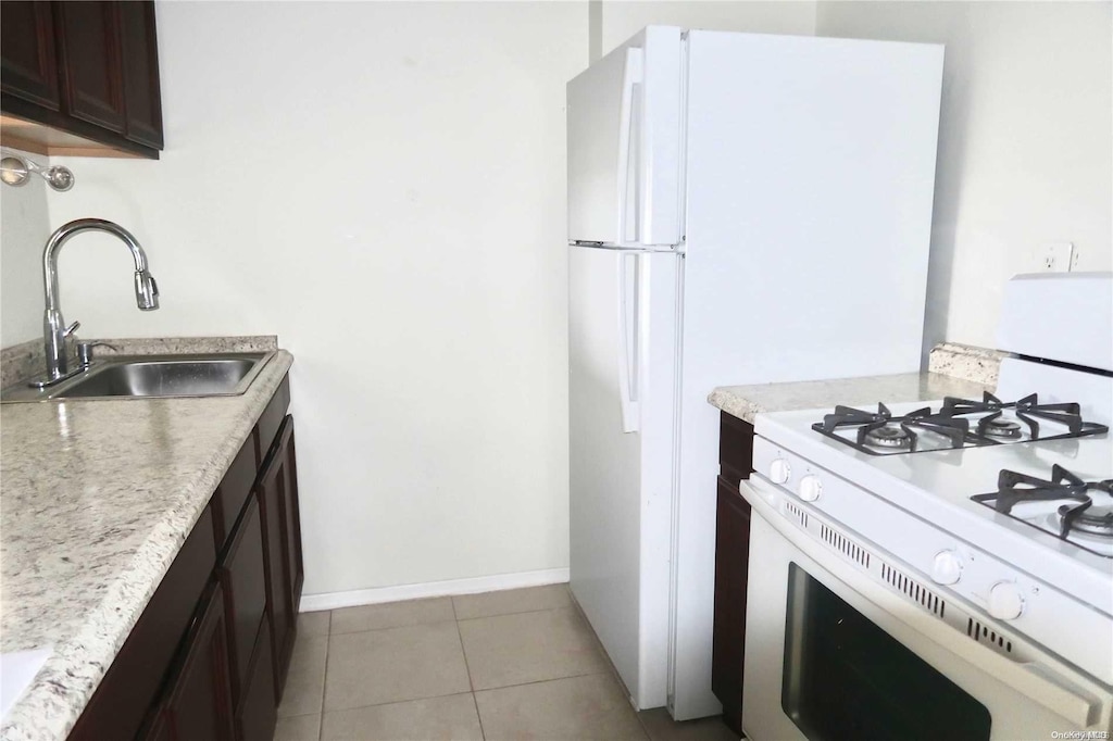 kitchen featuring light tile patterned flooring, dark brown cabinetry, white gas stove, and sink