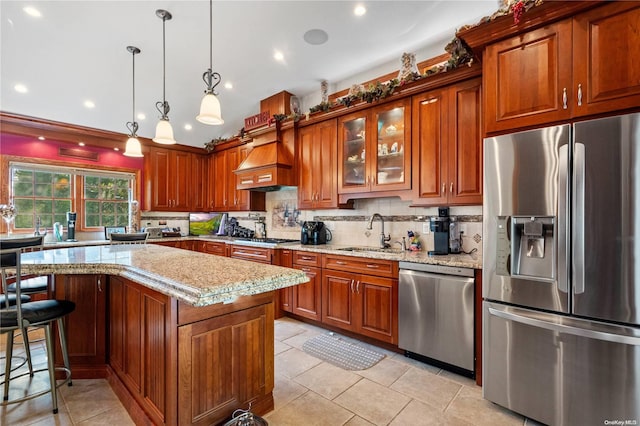 kitchen featuring light stone counters, decorative light fixtures, appliances with stainless steel finishes, custom range hood, and a kitchen island