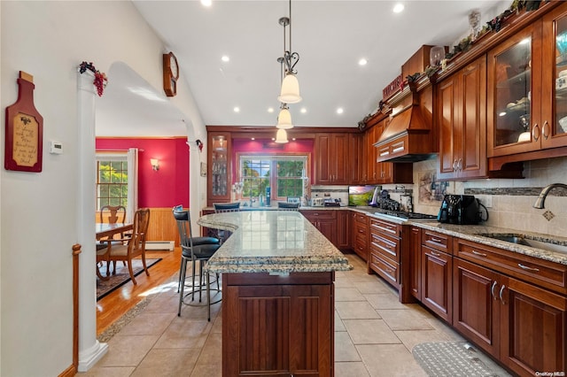 kitchen with sink, hanging light fixtures, light stone counters, a kitchen island, and stainless steel gas stovetop