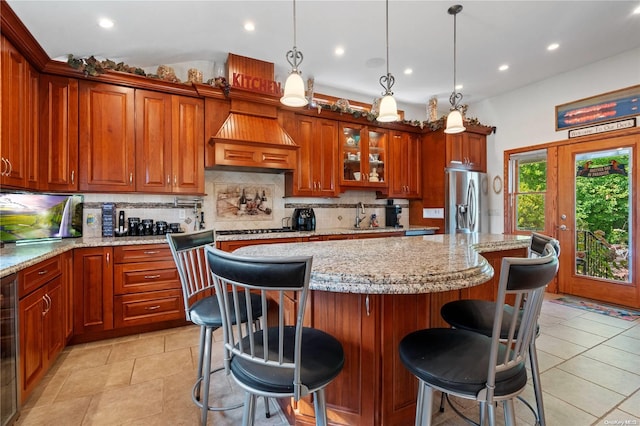 kitchen with a kitchen island, decorative light fixtures, a breakfast bar area, stainless steel fridge with ice dispenser, and custom range hood