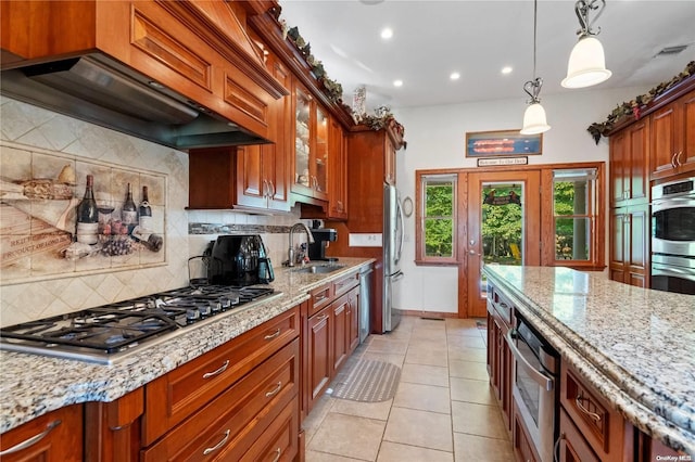 kitchen featuring premium range hood, sink, appliances with stainless steel finishes, pendant lighting, and light stone countertops