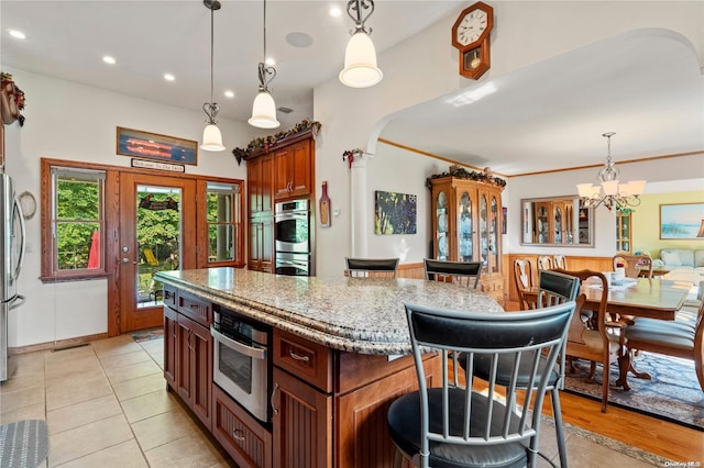 kitchen with a breakfast bar, decorative light fixtures, a center island, stainless steel appliances, and light stone countertops