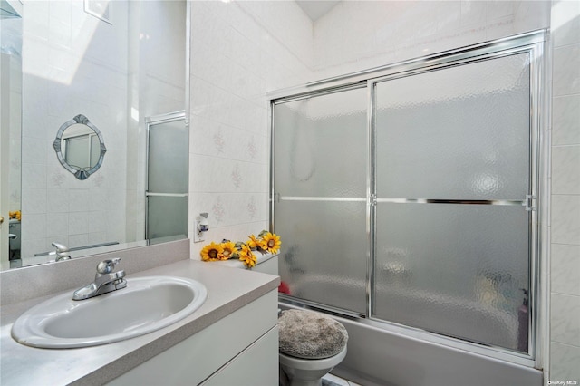 full bathroom featuring vanity, tile walls, shower / bath combination with glass door, and toilet