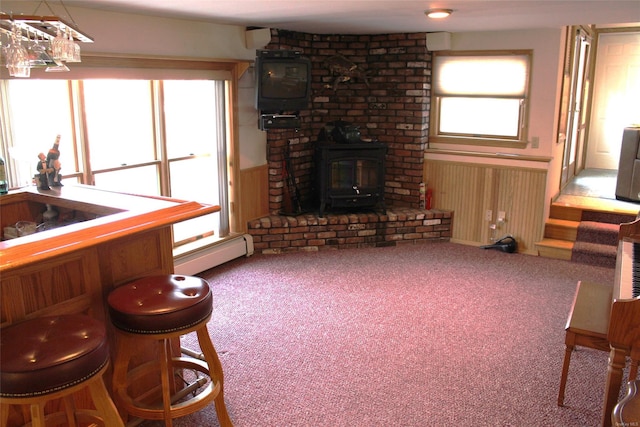 carpeted living room with baseboard heating, a healthy amount of sunlight, and a wood stove