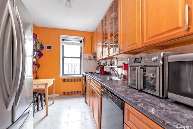 bar featuring appliances with stainless steel finishes, sink, light tile patterned floors, dark stone countertops, and radiator heating unit