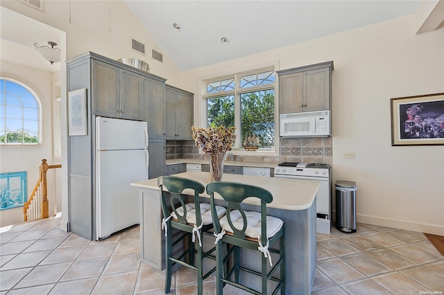 kitchen with a breakfast bar, a wealth of natural light, a center island, and white appliances