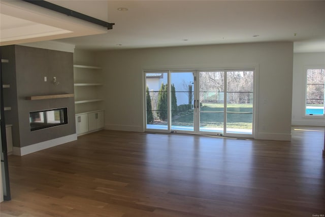 unfurnished living room featuring dark hardwood / wood-style flooring, a healthy amount of sunlight, and built in shelves