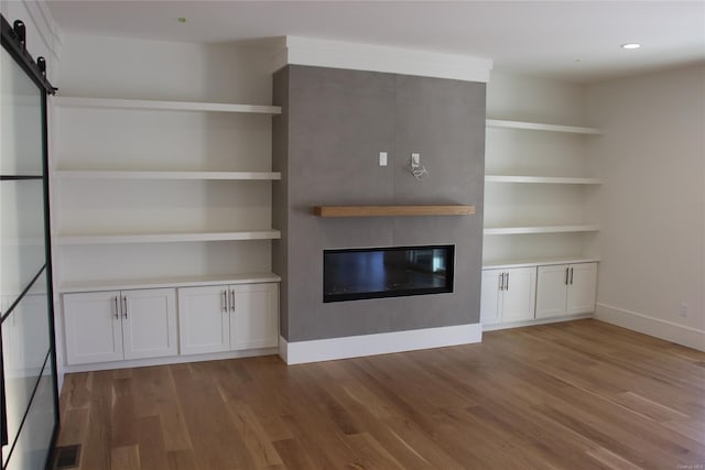 unfurnished living room with wood-type flooring, a barn door, and a fireplace