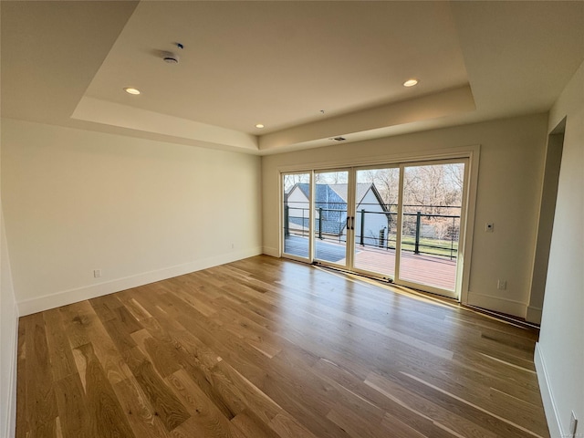 empty room with wood-type flooring and a tray ceiling