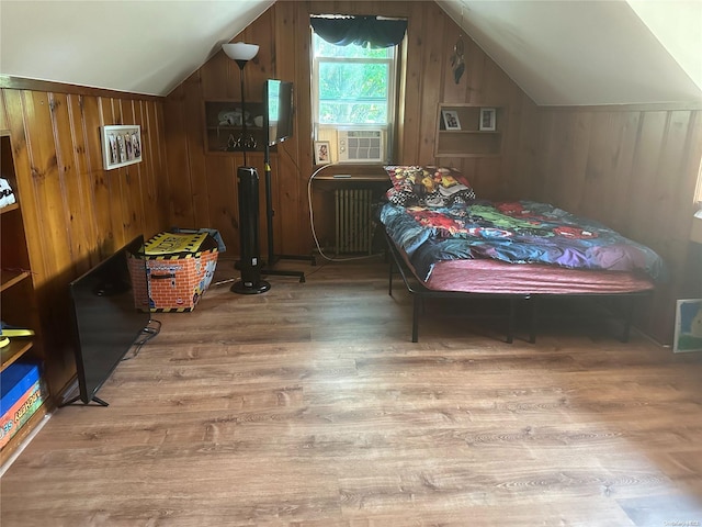 bedroom featuring radiator heating unit, a wall mounted air conditioner, hardwood / wood-style floors, vaulted ceiling, and wooden walls