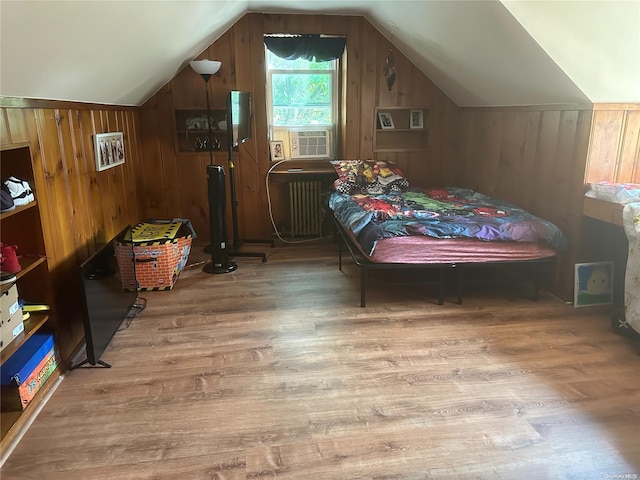 bedroom with light wood-type flooring, vaulted ceiling, radiator, and wooden walls