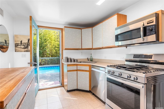 kitchen featuring sink, light tile patterned flooring, stainless steel appliances, and wood counters