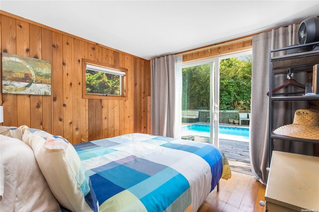 bedroom with access to exterior, light hardwood / wood-style flooring, multiple windows, and wooden walls