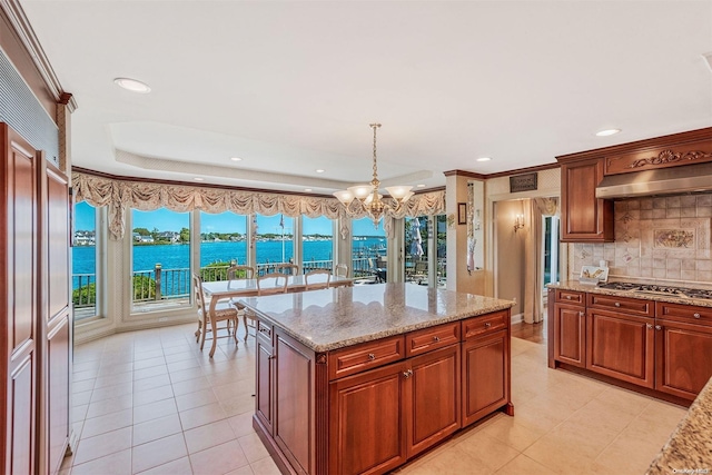 kitchen featuring exhaust hood, a water view, decorative light fixtures, a kitchen island, and stainless steel gas cooktop