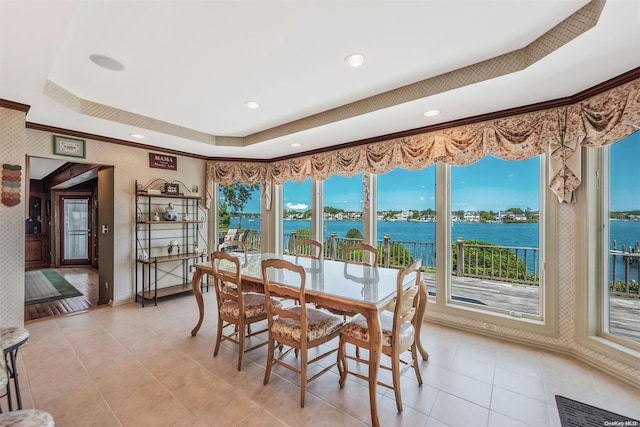 tiled dining area with a raised ceiling, a water view, and ornamental molding