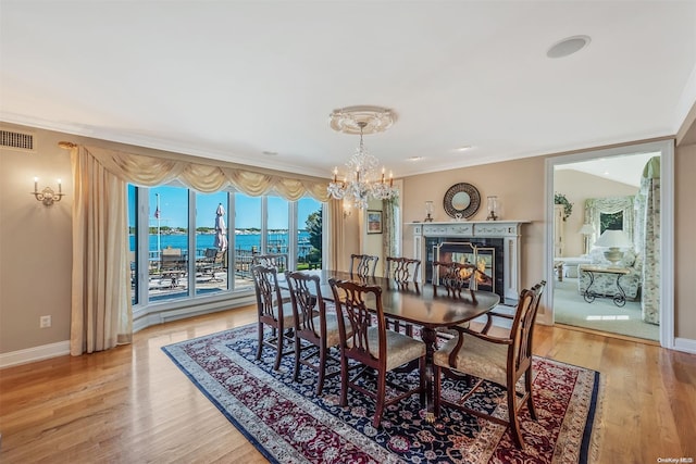 dining room with a chandelier, a water view, ornamental molding, and light hardwood / wood-style flooring