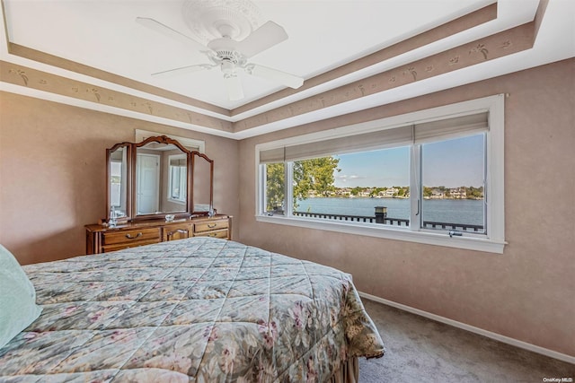 carpeted bedroom with a tray ceiling, ceiling fan, and a water view