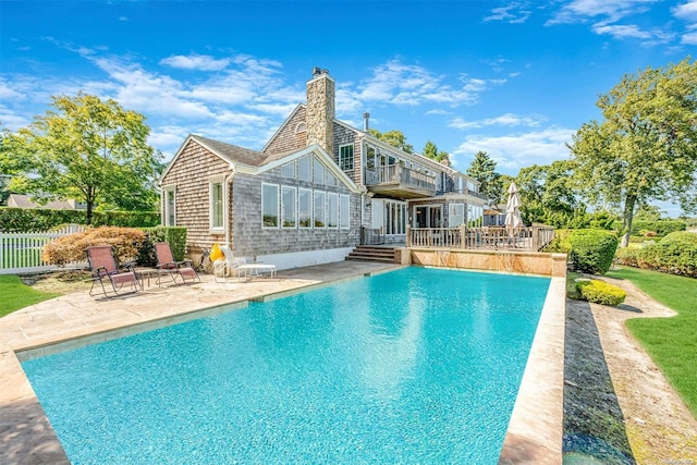 rear view of house featuring a fenced in pool, a balcony, and a patio