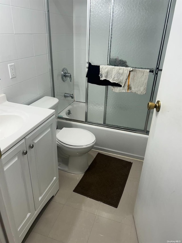 full bathroom featuring vanity, bath / shower combo with glass door, tile patterned flooring, toilet, and tile walls