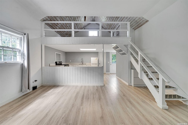 unfurnished living room featuring light wood-type flooring, vaulted ceiling, and sink