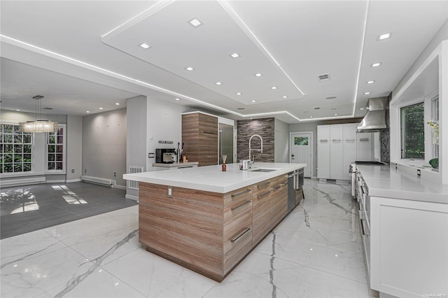 kitchen featuring white cabinetry, a large island, sink, a baseboard radiator, and wall chimney range hood