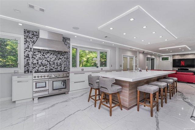 kitchen with wall chimney exhaust hood, a breakfast bar, white cabinets, and double oven range