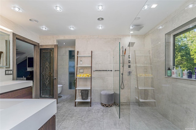 bathroom featuring tiled shower, vanity, tile walls, and toilet