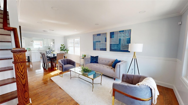 living area featuring light wood-type flooring, crown molding, baseboards, and stairs