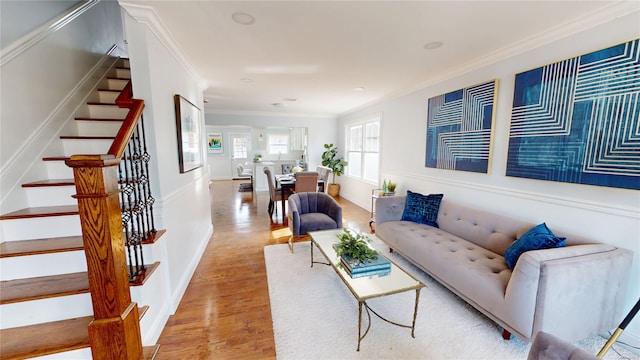 living area featuring stairs, ornamental molding, light wood-type flooring, and baseboards