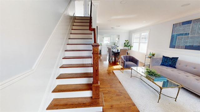 stairway with crown molding and wood finished floors