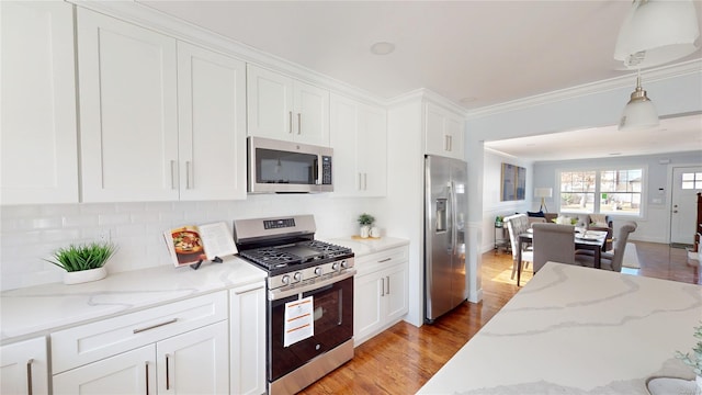 kitchen with appliances with stainless steel finishes, ornamental molding, open floor plan, white cabinetry, and light wood-type flooring