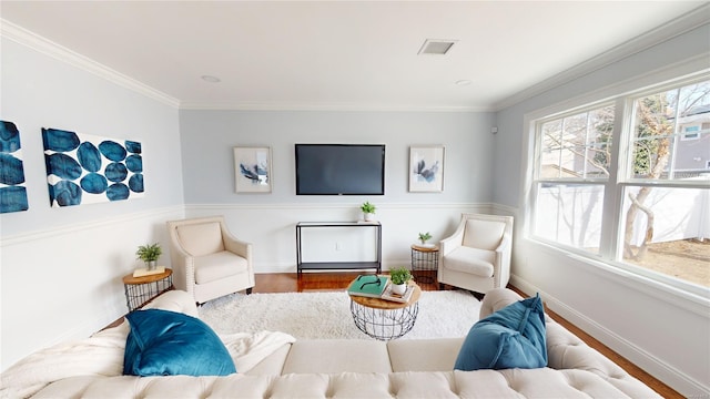 living area featuring baseboards, visible vents, wood finished floors, and ornamental molding