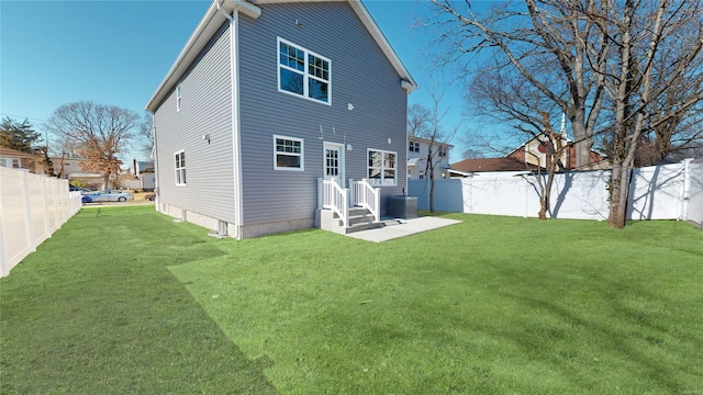 rear view of property with a fenced backyard, a lawn, and central AC