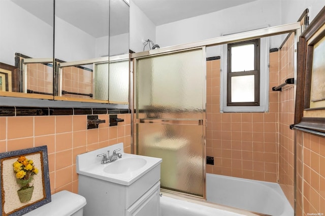 full bathroom with shower / bath combination with glass door, vanity, toilet, and tile walls