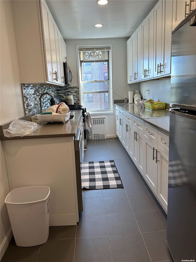 kitchen featuring radiator, dark tile patterned flooring, white cabinets, and appliances with stainless steel finishes