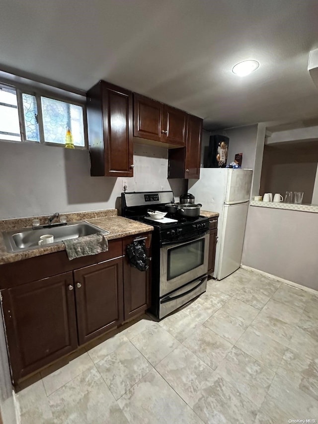 kitchen featuring dark brown cabinetry, sink, white fridge, and stainless steel range with gas stovetop