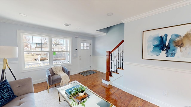 living area featuring a wainscoted wall, wood finished floors, visible vents, stairs, and crown molding