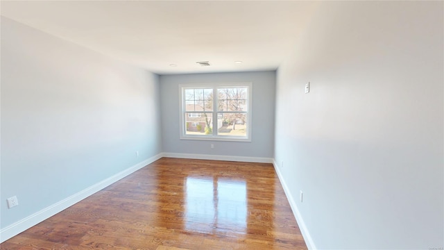 spare room with wood finished floors, visible vents, and baseboards