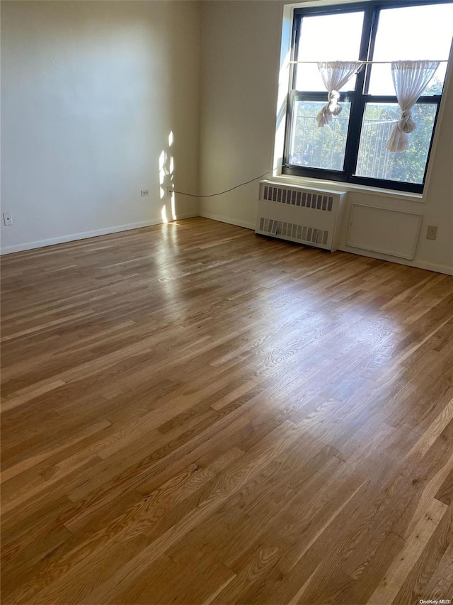 unfurnished room featuring radiator heating unit and hardwood / wood-style floors