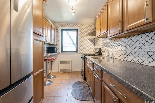 kitchen featuring radiator, sink, decorative backsplash, light tile patterned floors, and appliances with stainless steel finishes