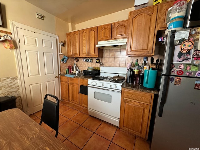 kitchen with white range with gas stovetop, backsplash, stainless steel refrigerator, and dark tile patterned floors