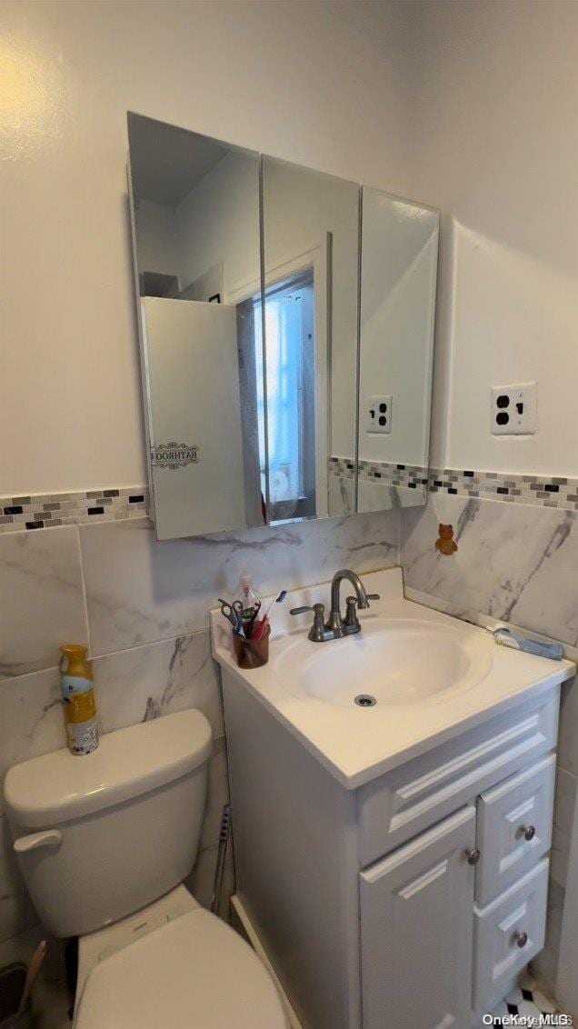 bathroom featuring vanity, toilet, and tile walls