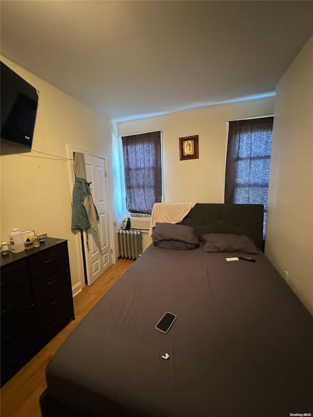 bedroom featuring light wood-type flooring, radiator heating unit, and multiple windows