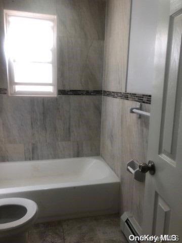 bathroom featuring a healthy amount of sunlight, toilet, baseboard heating, and shower / washtub combination