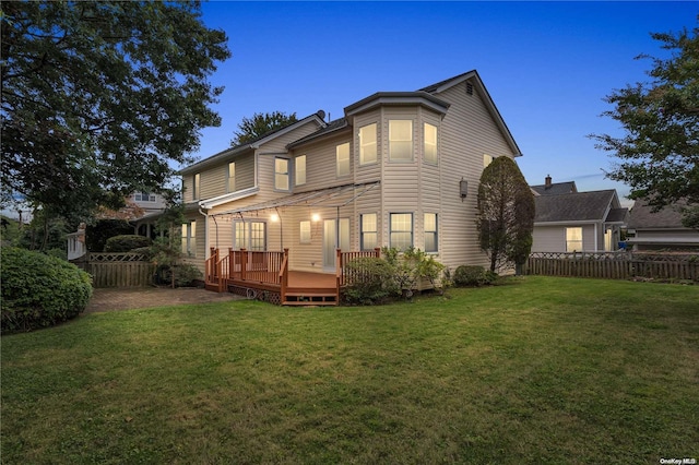 back house at dusk featuring a lawn and a deck